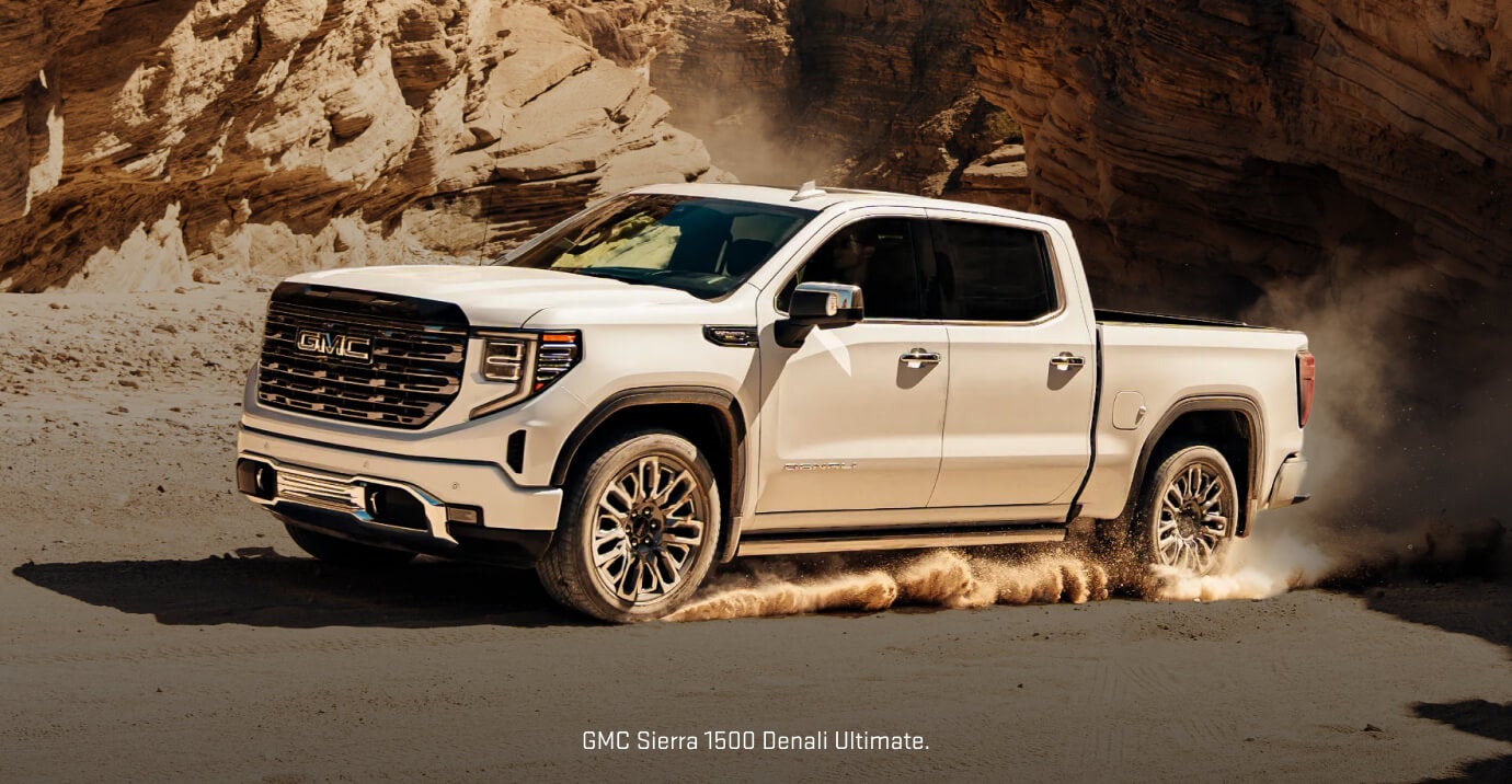 Front-three-quarter view of a White 2026 GMC Sierra 1500 Denali Ultimate kicking up desert dust.