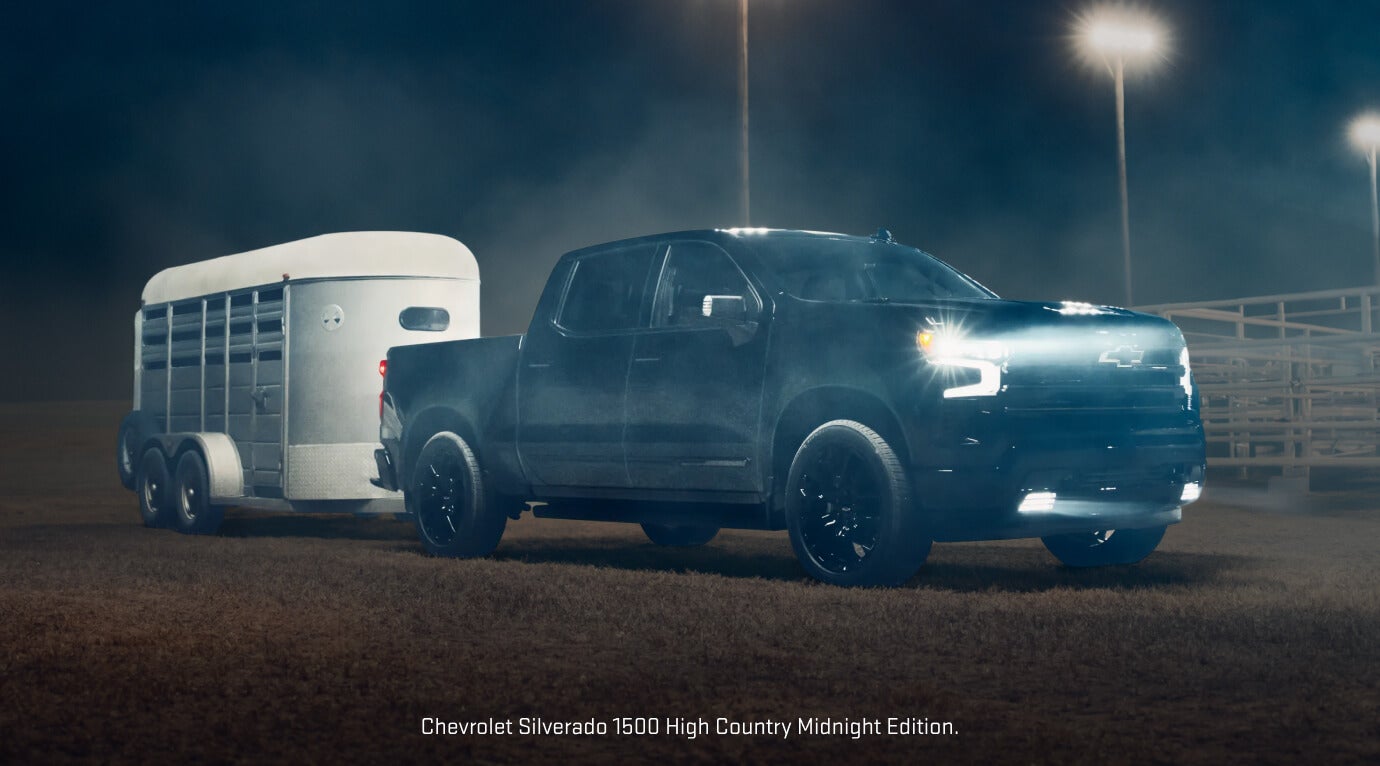 Front-three-quarter view of a Black 2026 Chevrolet Silverado 1500 High Country Midnight Edition towing a horse trailer.
