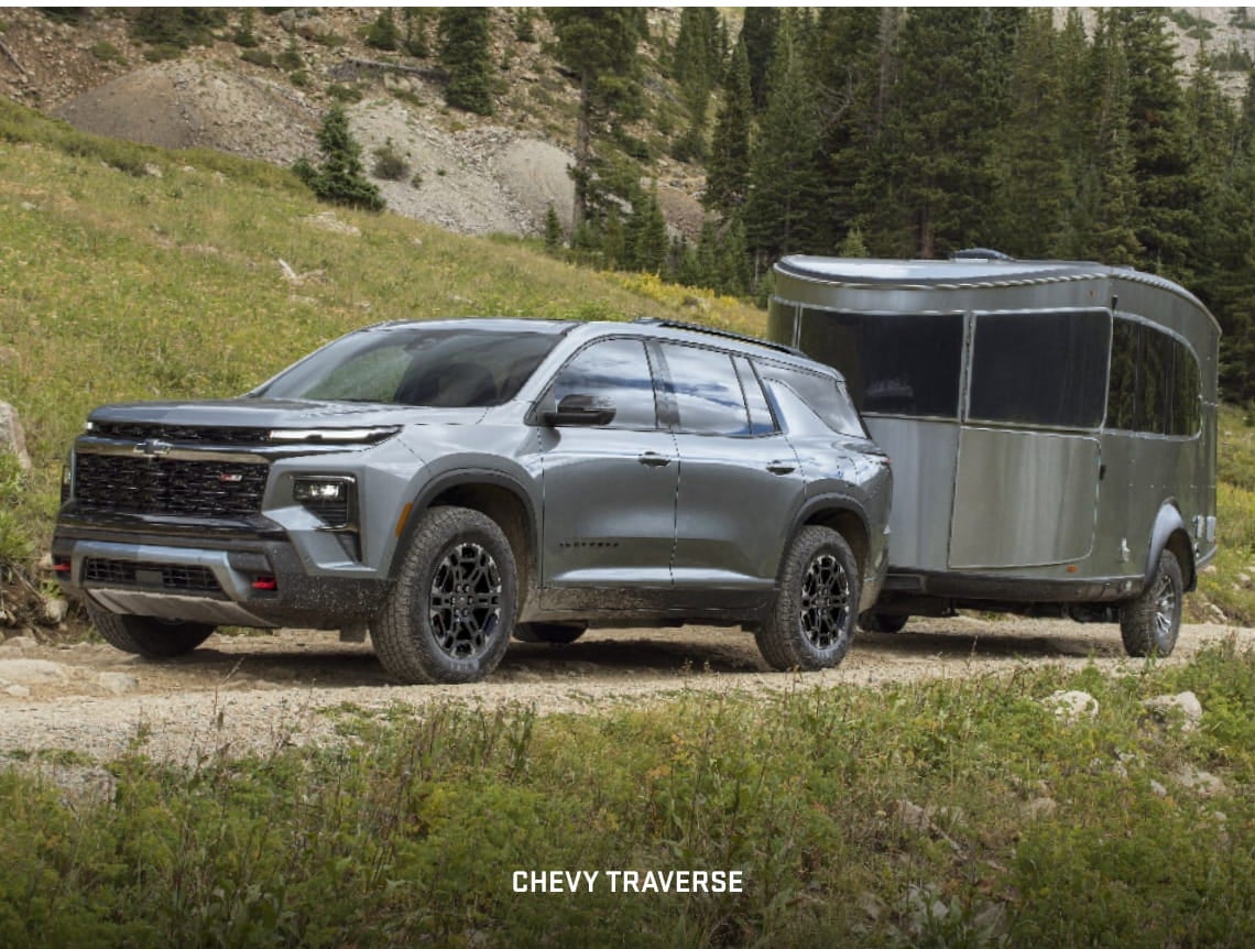 Gray Chevrolet Traverse towing a travel trailer on a rugged mountain trail.